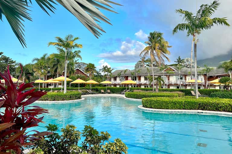 Tropical resort pool with yellow umbrellas, palm trees, and mountain views