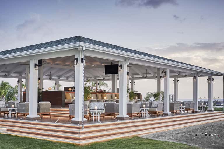 Covered oceanfront pavilion with white columns, dark roof, lounge seating, and water views