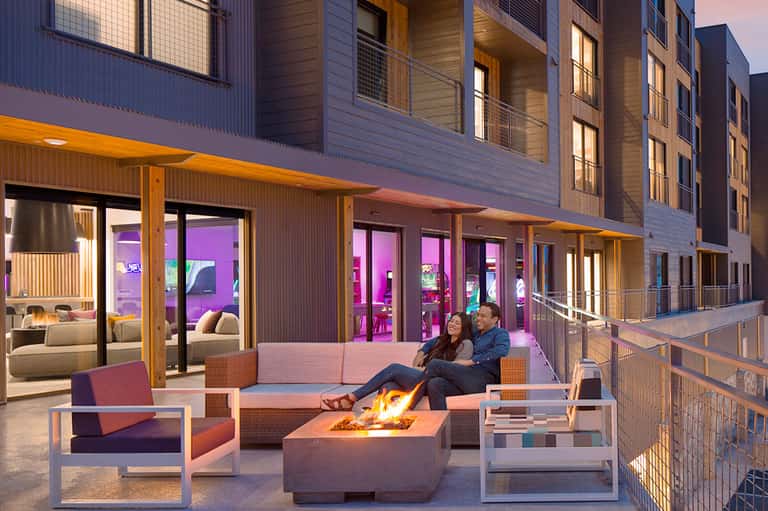 Outdoor terrace with fire pit, seating area, and modern apartment building at dusk
