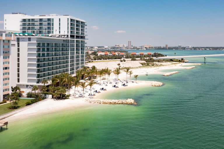 Beachfront hotel towers above turquoise waters and white sand beach with lounging guests