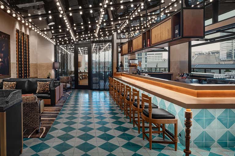 Modern hotel bar with marquee lighting, turquoise tile floor, and city skyline views