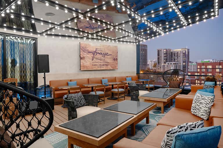 Rooftop lounge with orange seating, string lights, and city skyline views at evening
