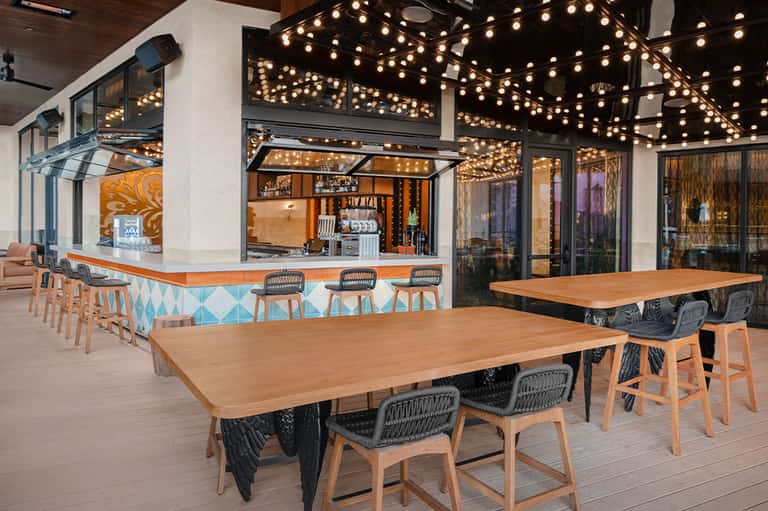 Modern outdoor dining area with wooden tables, decorative lighting, and ocean-view bar