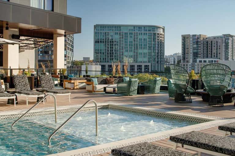 Urban rooftop spa area with hot tub, lounge seating, fire pit, and downtown cityscape views