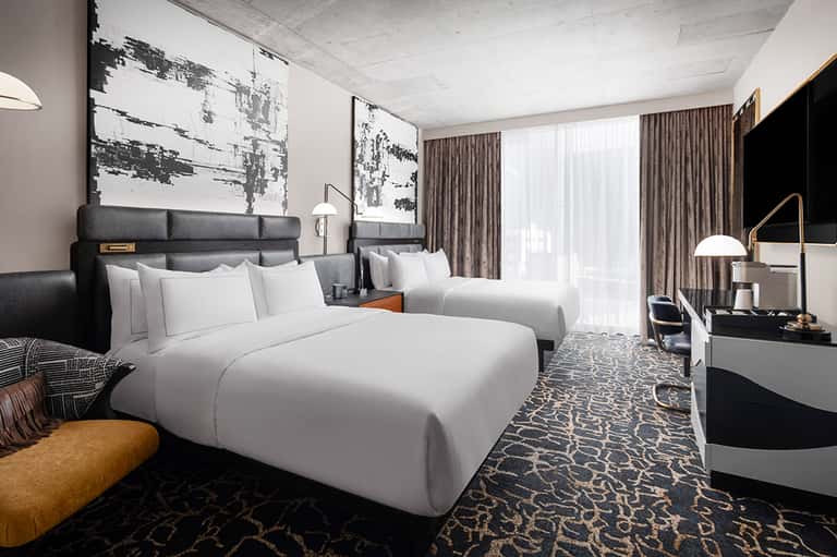 Contemporary hotel room with two queen beds, gray headboards, patterned rug, and balcony access