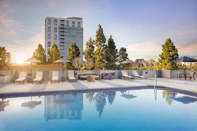Modern rooftop pool with white lounge chairs, fire pit, and city views at dusk