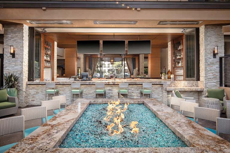 Modern outdoor bar with stone fireplace, turquoise fire feature, and lounge seating area