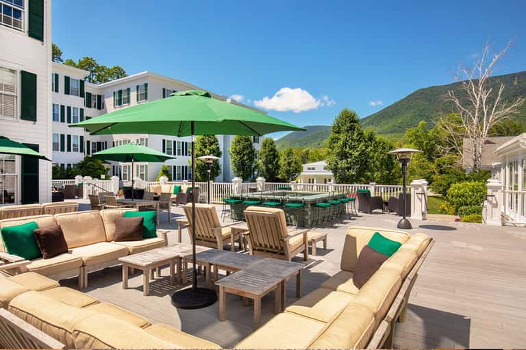 Resort terrace with cream furniture, green umbrellas, and mountain backdrop