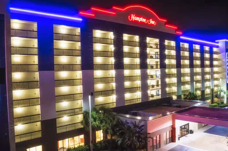 Hampton Inn hotel exterior at night with blue neon trim, illuminated signage, and palm trees