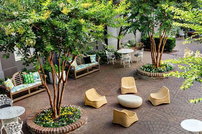 Courtyard seating area with wicker chairs, potted plants, and mature trees overhead