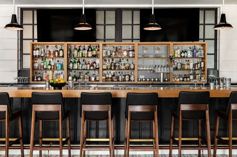 Modern bar counter with wooden seating and extensive spirit bottle collection on backlit shelves