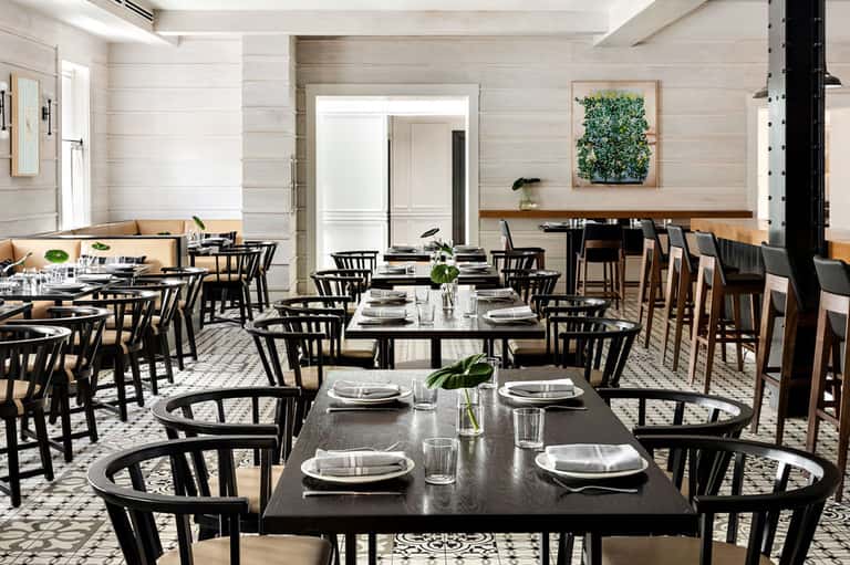 Fine dining restaurant with black chairs, long tables, white linens, and modern minimalist design
