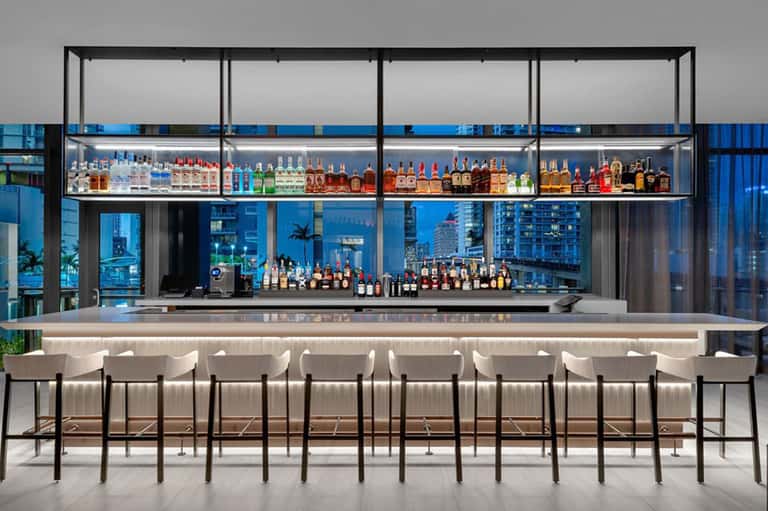 Upscale bar with extensive spirit collection, white bar seating, and city window views