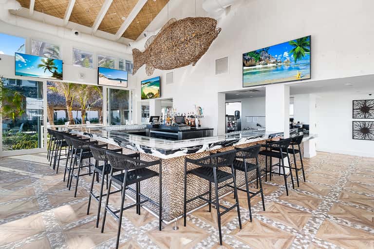 Contemporary beach club bar with modern furniture, large windows, and tropical decor