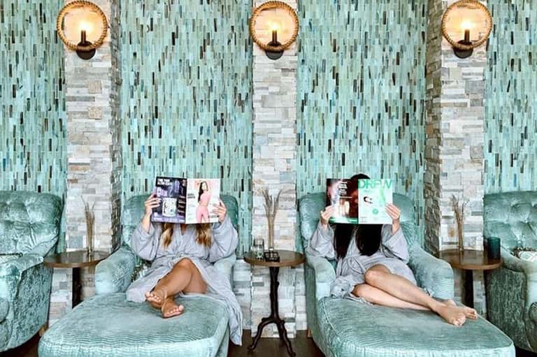 Spa relaxation lounge with turquoise velvet recliners, reading materials, and brass sconces
