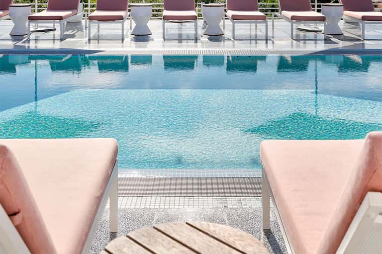 Modern pool deck with pink lounge chairs, turquoise water, and white seating area