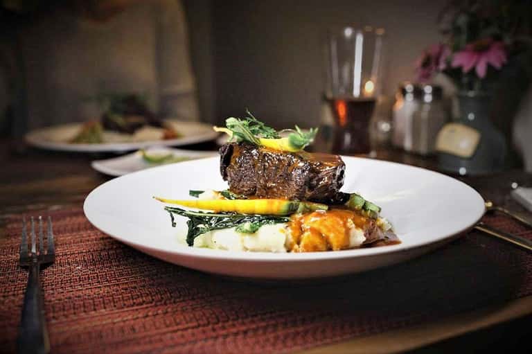 Plated fine dining steak with vegetables and garnish on white plate in elegant restaurant setting