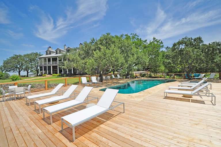 Resort pool deck with lounge chairs, vintage plantation house, and mature shade trees
