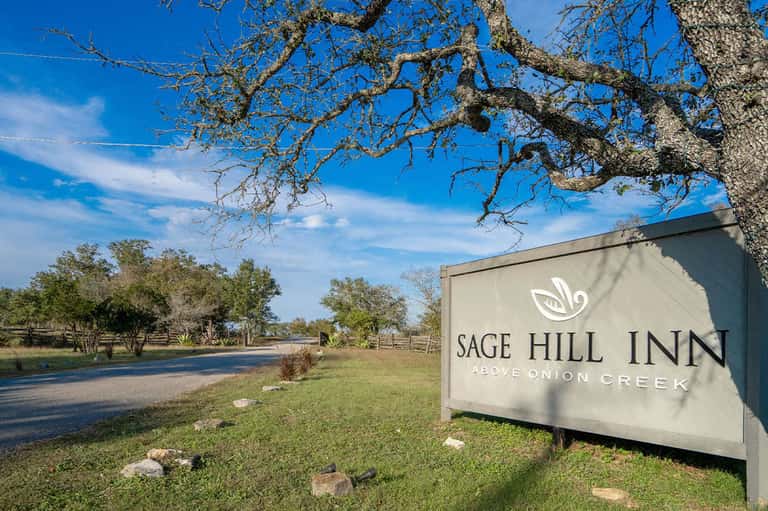 Sage Hill Inn entrance sign on rural grounds with trees and creek landscape