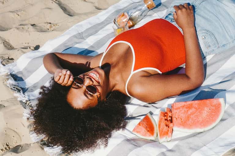 Woman relaxing on beach with watermelon slices and sunglasses on striped towel