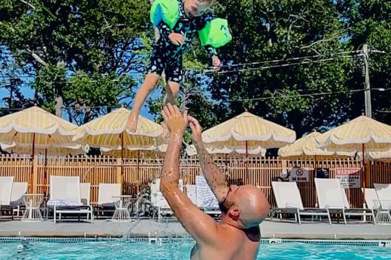 Adult and child playing in resort pool under yellow umbrellas on sunny afternoon
