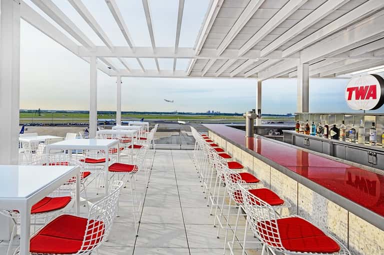 Rooftop dining terrace with red-seated chairs and aircraft runway views