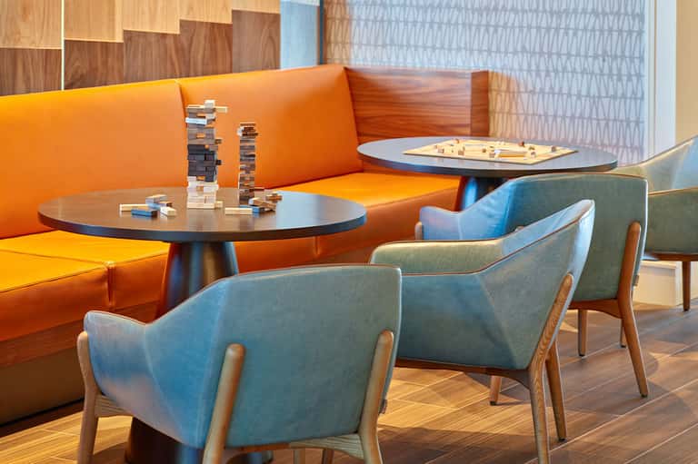 Contemporary lounge area with orange sofa, blue chairs, and game tables