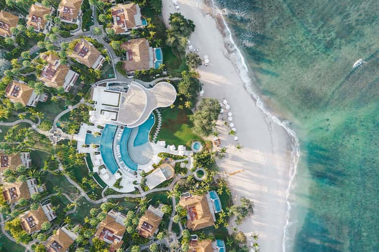 Aerial view of coastal resort with curved pools, white buildings, private beach, and turquoise ocean
