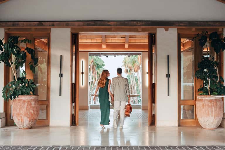 Couple walking through modern hotel lobby with wooden beams and palm tree views
