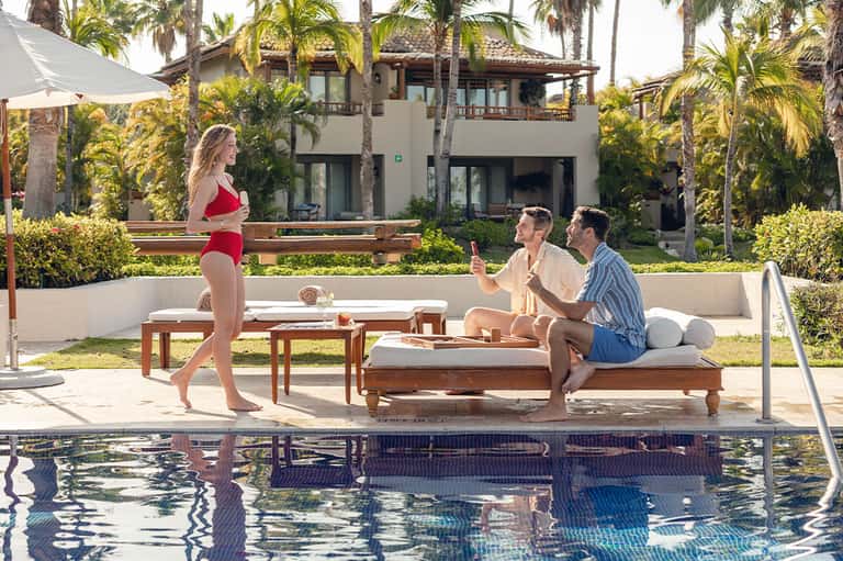 Resort poolside with guests relaxing, palm trees, and modern villa backdrop