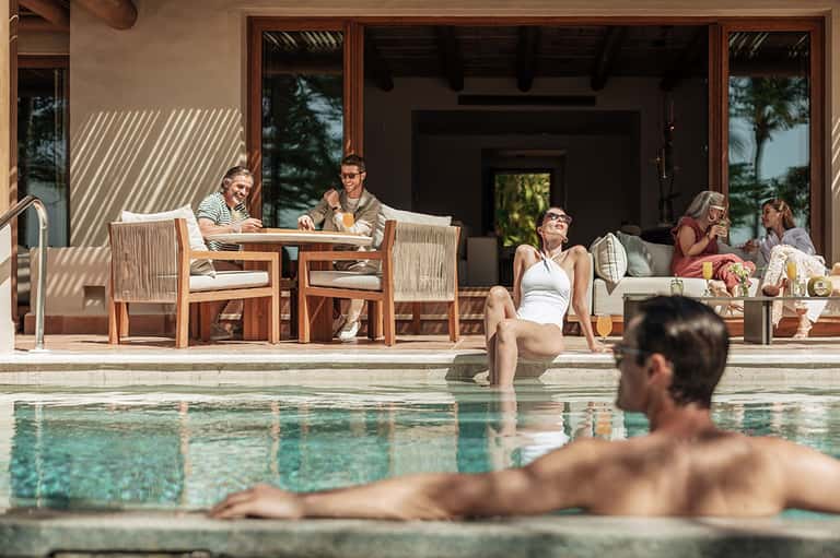 Resort poolside lounge area with guests relaxing on wooden deck and furniture