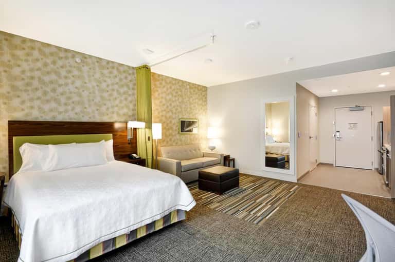 Spacious hotel suite with king bed, sitting area, patterned wallpaper, and modern furnishings