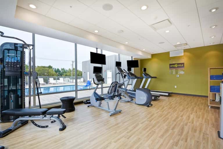 Modern fitness center with exercise equipment, large windows overlooking pool, and yellow accent wall