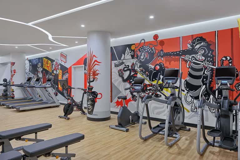 Modern fitness center with treadmills, exercise bikes, and vibrant red and black street art mural