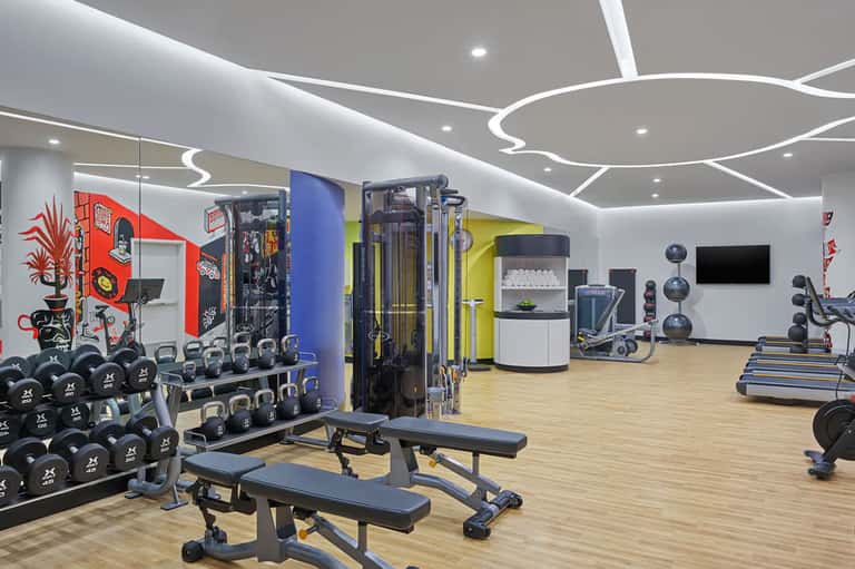Modern fitness center with colorful accent walls, weight rack, exercise machines, free weights, and contemporary ceiling design