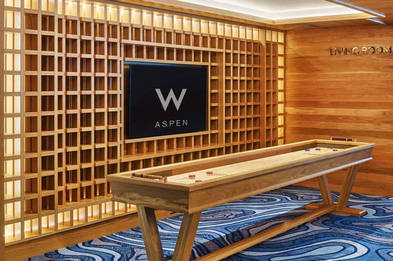 Hotel game room with air hockey table, TV displaying W Aspen logo, and wooden wall paneling