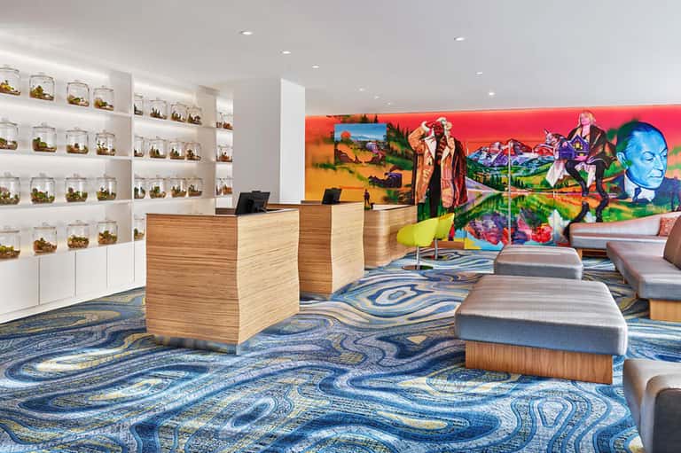 Modern hotel lobby with colorful abstract wall art, wooden reception desk, and blue patterned carpet