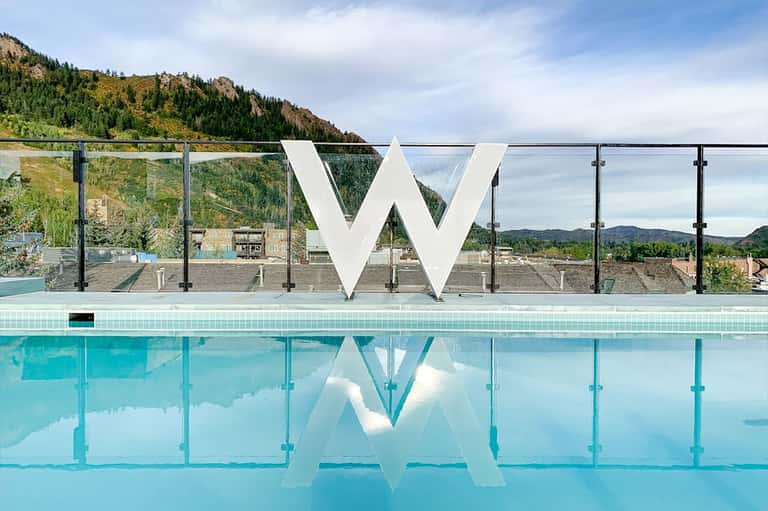 W hotel pool with large white logo, glass railings, and mountain landscape backdrop