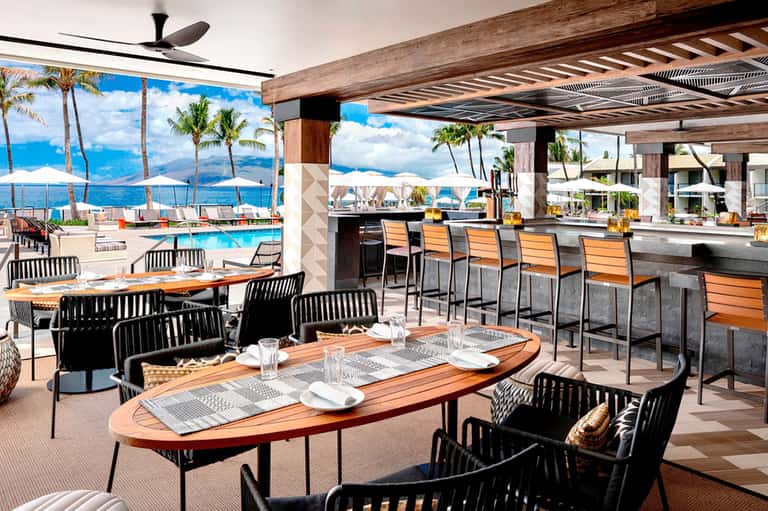 Upscale poolside restaurant with ocean view, wood tables, modern furniture, and bar seating