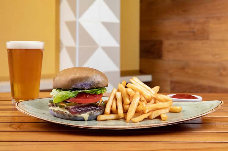 Burger with fries and beer on wooden table in warm-toned dining area