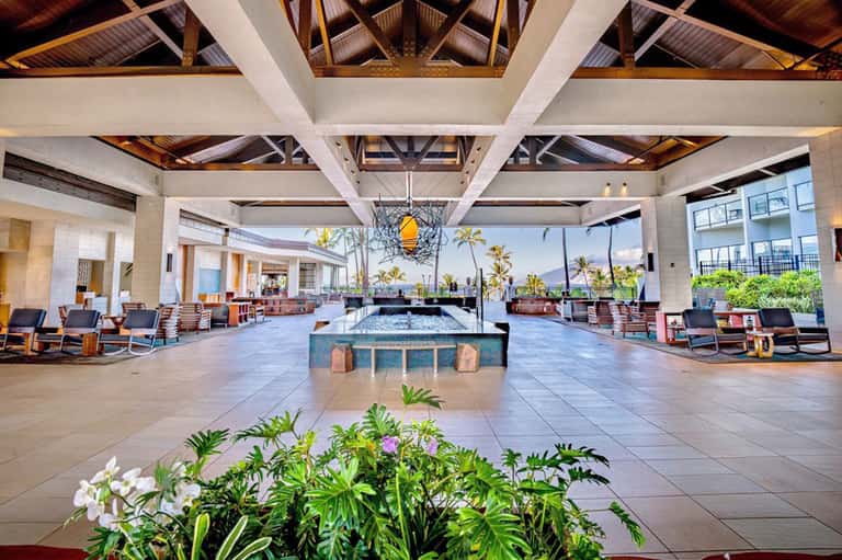 Grand resort lobby with central water feature and ocean view through columns