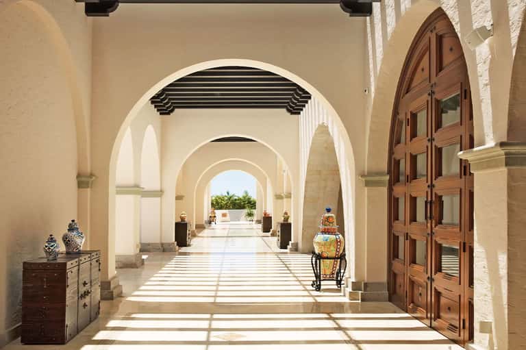 Arched hallway with cream columns, wooden doors, and decorative urns