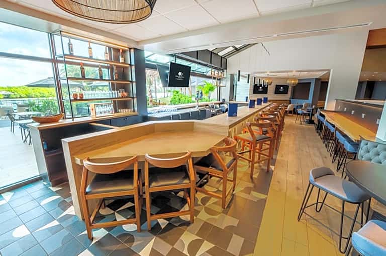 Modern hotel bar with wooden counter, stools, and floor-to-ceiling windows overlooking landscape