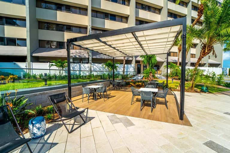 Contemporary poolside patio with pergola shade structure, seating, and ocean view backdrop
