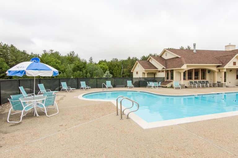 Resort pool with blue lounge chairs, umbrella, and large residential building