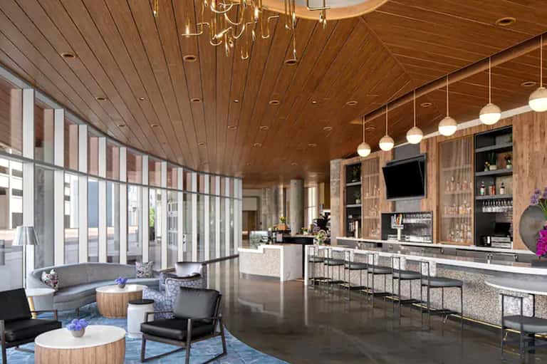 Modern hotel bar with wooden ceiling, contemporary seating, full bar shelving, and large windows