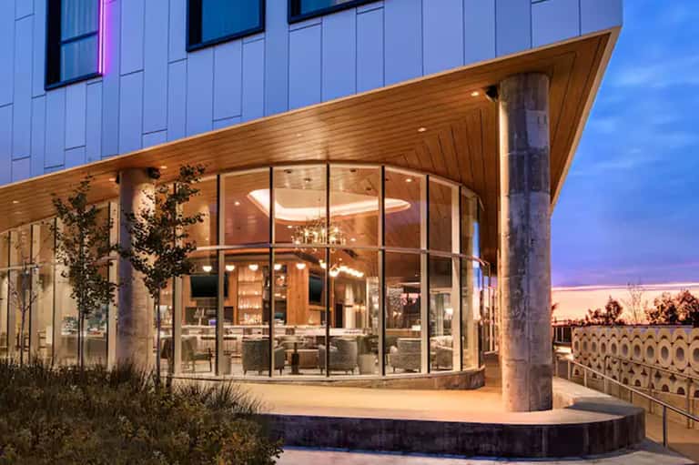 Modern architectural entrance at dusk with curved wooden ceiling, glass walls, and illuminated interior