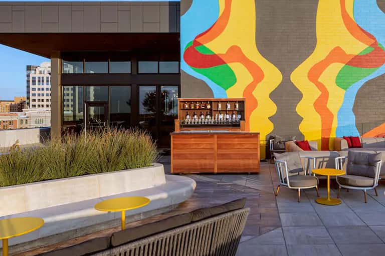 Rooftop bar area with vibrant mural art, wooden bar counter, seating, and city views