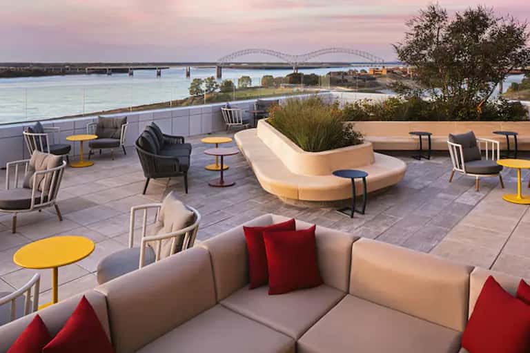 Rooftop terrace at dusk with modern seating, yellow accent tables, and bridge views over water