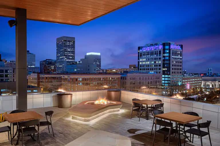Urban rooftop terrace with fire pit, modern seating, and city skyline illuminated at dusk